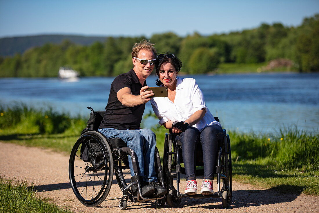 Couple in wheelchairs making selfie photo on the Main, Großwallstadt, Spessart-Mainland, Franconia, Bavaria, Germany, Europe