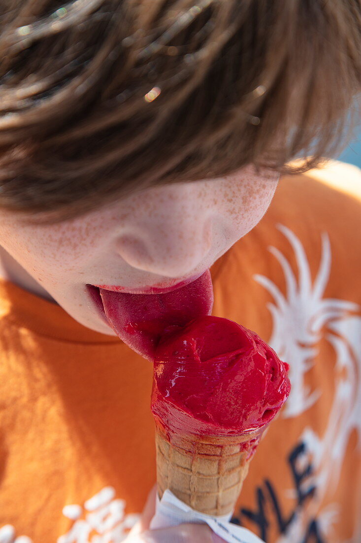 Junge mit roter Zunge genießt Eiswaffel mit Kugel Himbeereis, Tauberbischofsheim, Baden-Württemberg, Deutschland, Europa