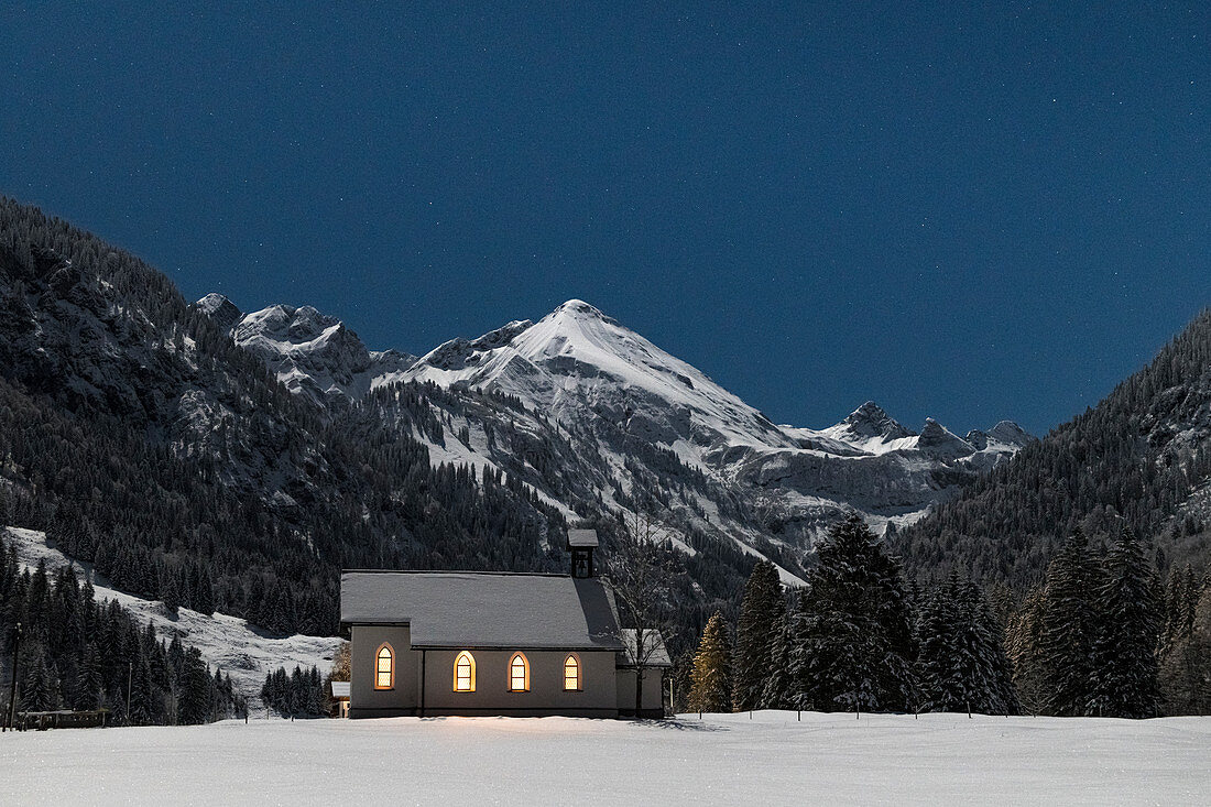 Church chapel in snowy winter landscape in front of mountain panorama at night, Germany, Bavaria, Oberallgäu, Oberstdorf