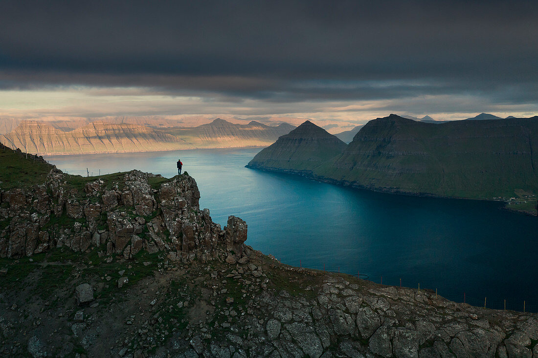 Hikers at Hvithamar near the town of Gjogv on the Faroe island of Eysturoy with a panoramic view of the fjord at sunset
