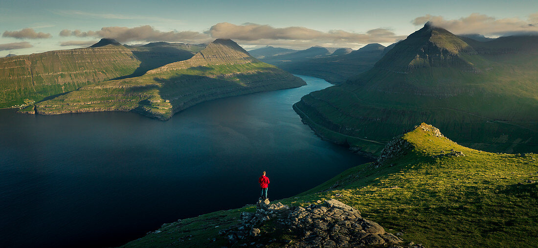 Man with a red jacket at Hvithamar near the town of Gjogv on the Faroe island of Eysturoy with a panoramic view of the fjord