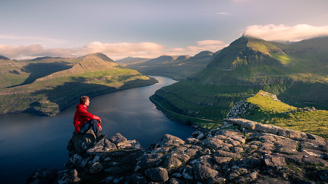 Man sitting at Hvithamar near the town of Gjogv on the Faroe island of Eysturoy with a panoramic view of the fjord