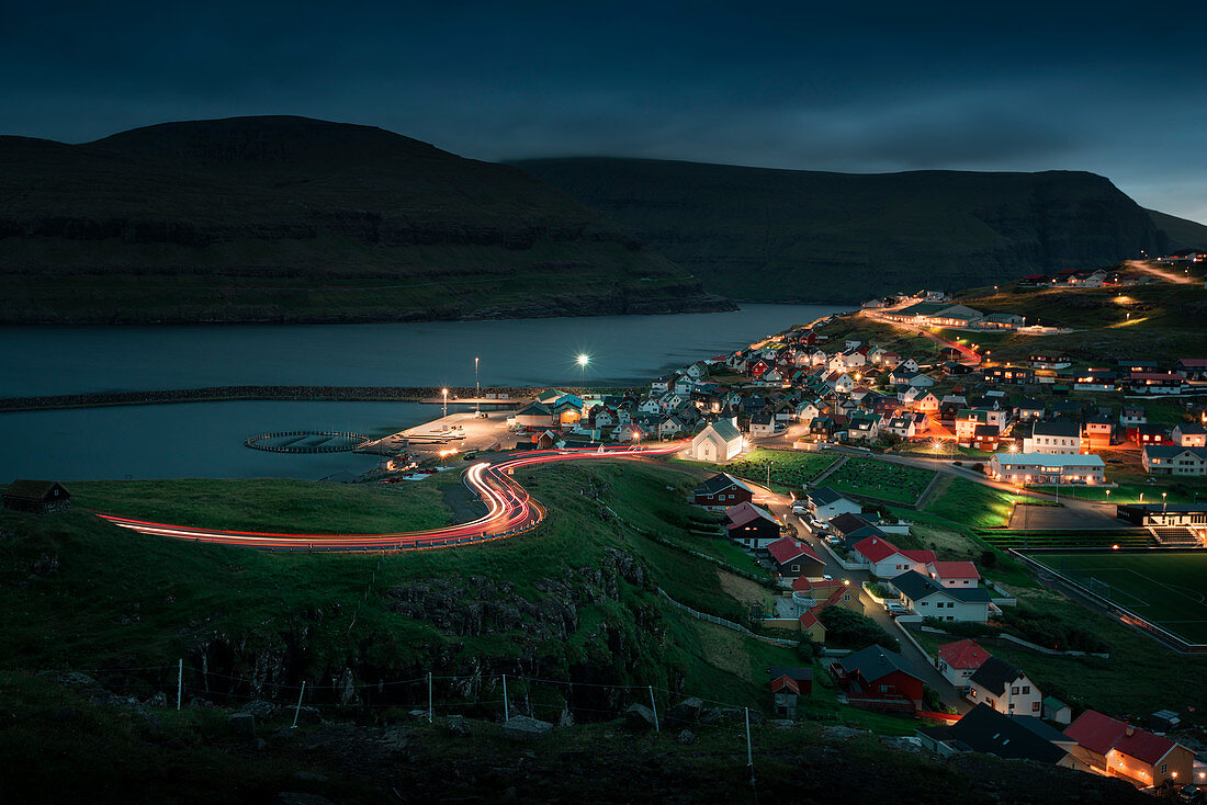 Dorf Eidi auf Eysturoy der Färöer Inseln bei Nacht mit geschwungener Straße und Autolichtern\n