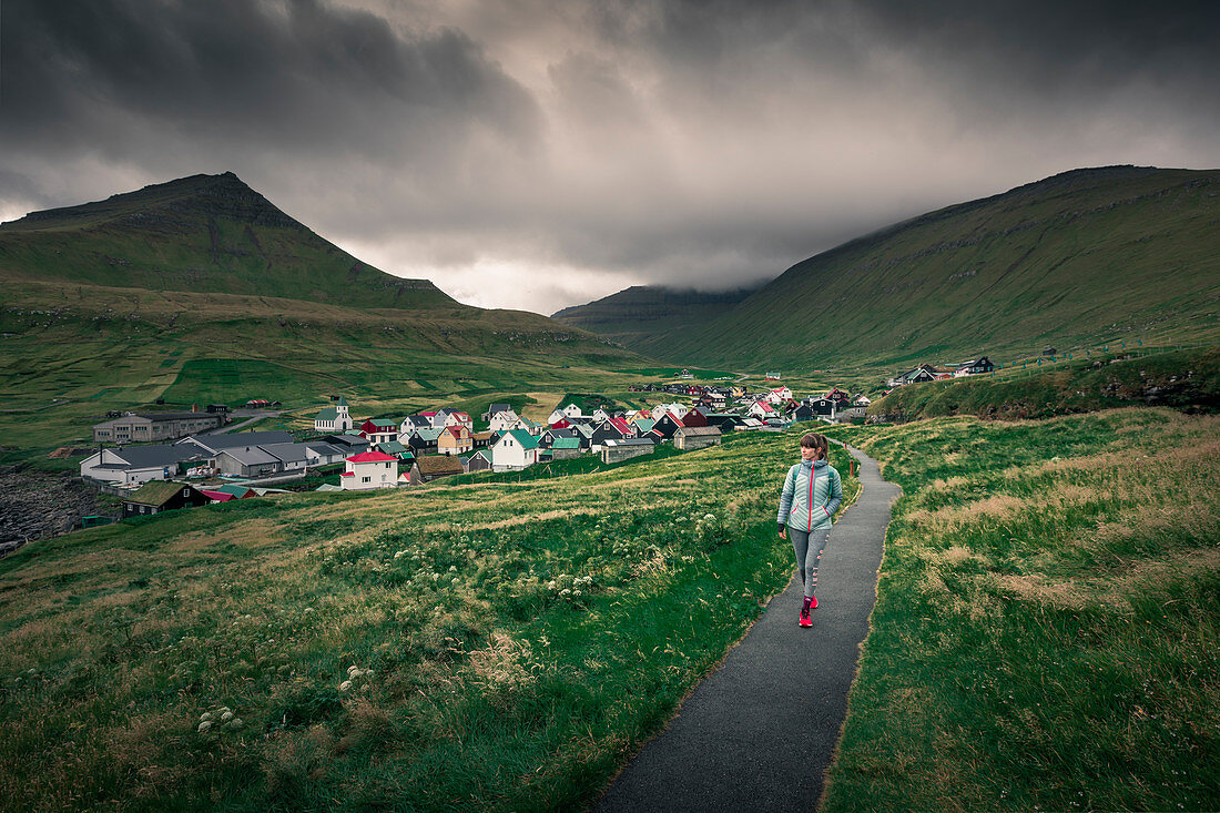 Woman walks on path in front of the village of Gjogv on Eysteroy, Faroe Islands