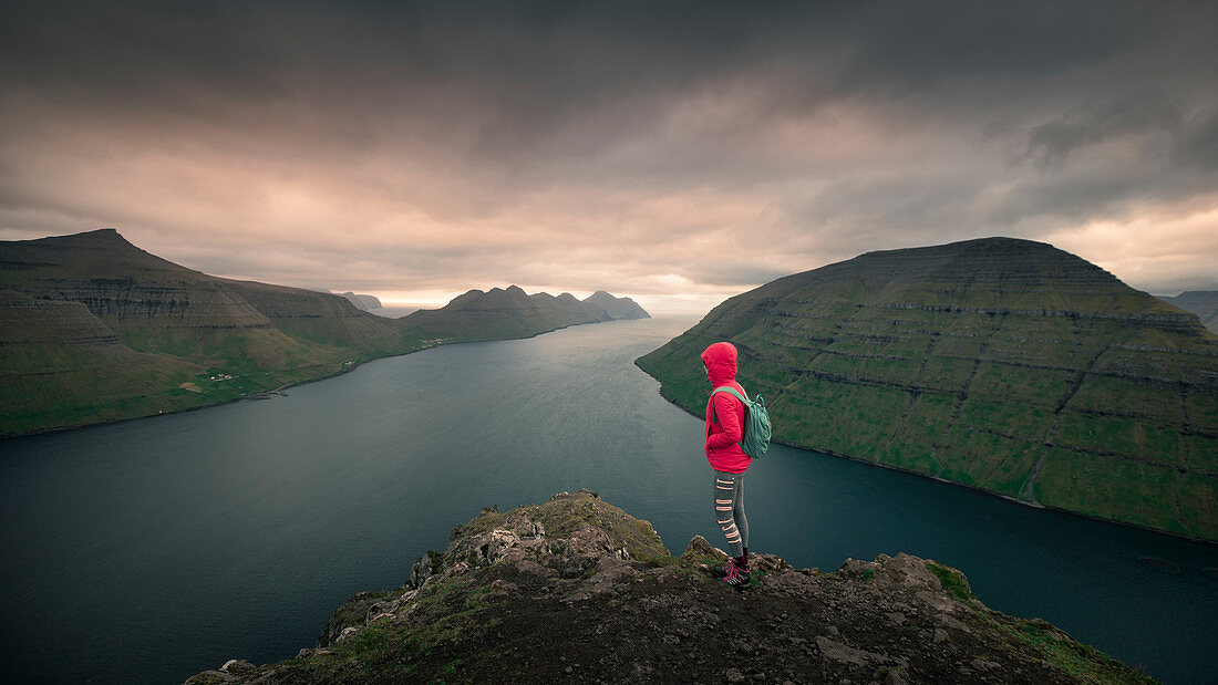 Woman at the Klakkur viewpoint near Klaksvik on the island of Bordaoy with a view of Klasoy and Kunoy in sunset, Faroe Islands