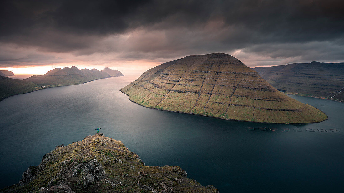 Man at the Klakkur viewpoint near Klaksvik on the island of Bordaoy with a view of Klasoy and Kunoy in sunset, Faroe Islands