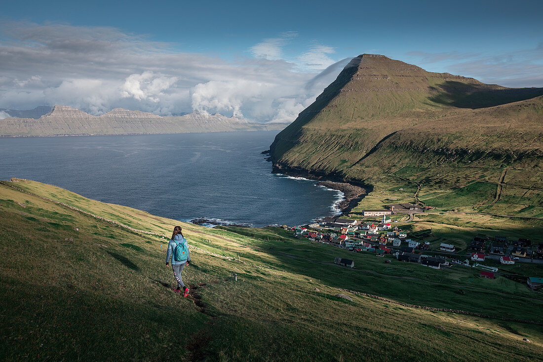 Woman hikes at the village of Gjogv on Eysteroy with gorge, sea and mountains, Faroe Islands