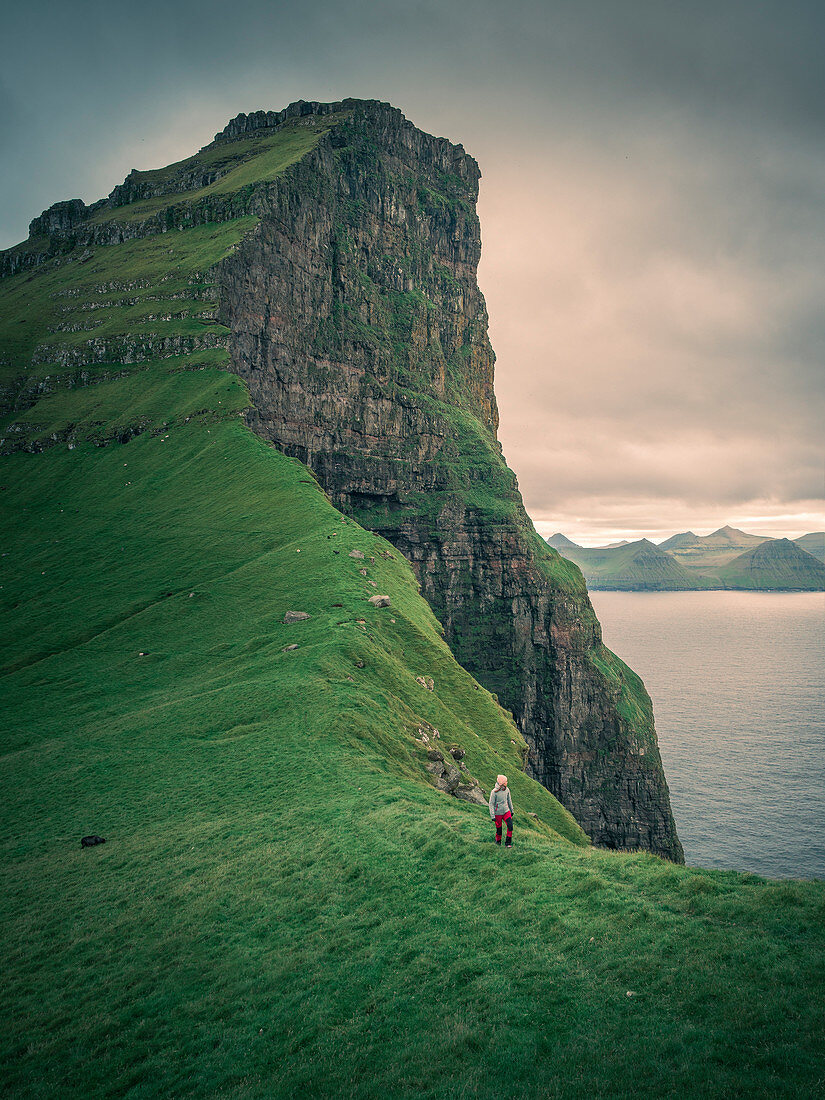 Woman hikes on cliff on Kalsoy Island, Faroe Islands
