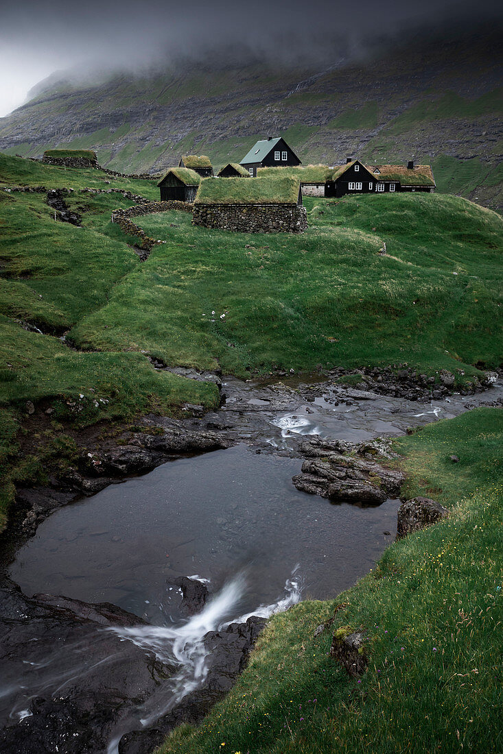 Hütten mit Grasdach und Fluss im Dorf Saksun auf der Insel Streymoy, Färöer Inseln\n