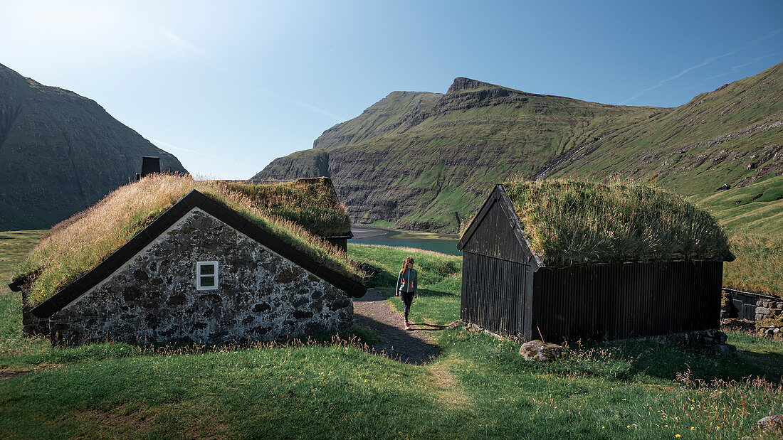 Frau bei Hütten mit Grasdach im Dorf Saksun auf der Insel Streymoy, Färöer Inseln\n