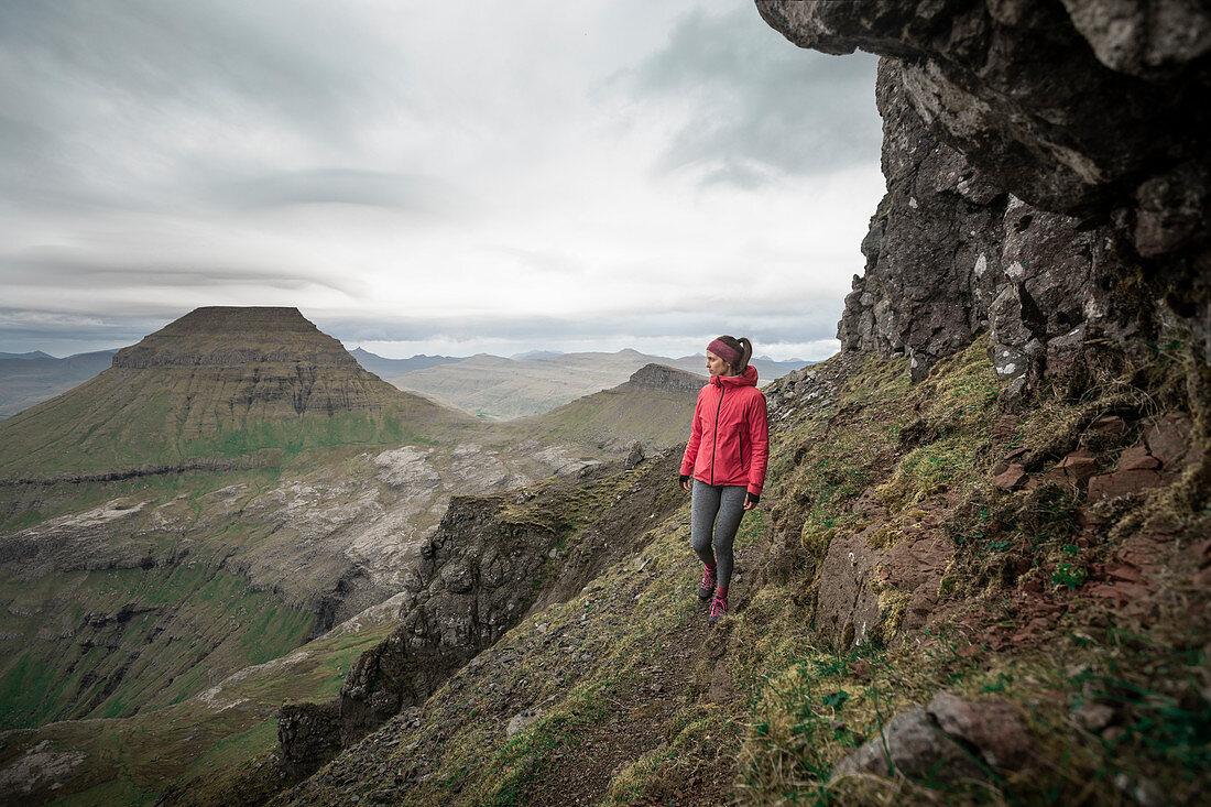 Frau wandert in der Landschaft der Färöer Inseln unter dramatischen Wolken \n