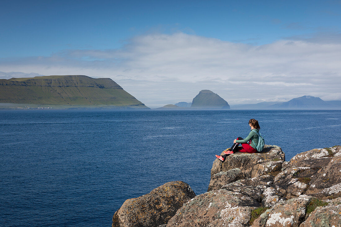 Frau an der Küste mit Blick auf Inseln der Färöer Inseln bei Sonne\n