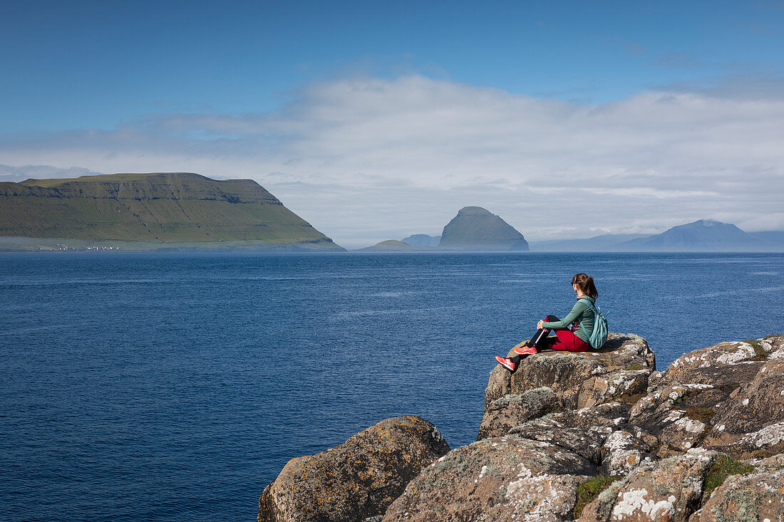 Woman on the coast overlooking islands of the Faroe Islands in sunshine