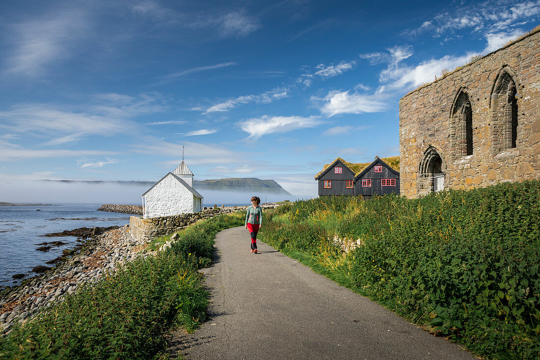 Frau wandert zu Kirche und Ruine im Dorf Kirkjubøur auf Streymoy, Färöer Inseln\n