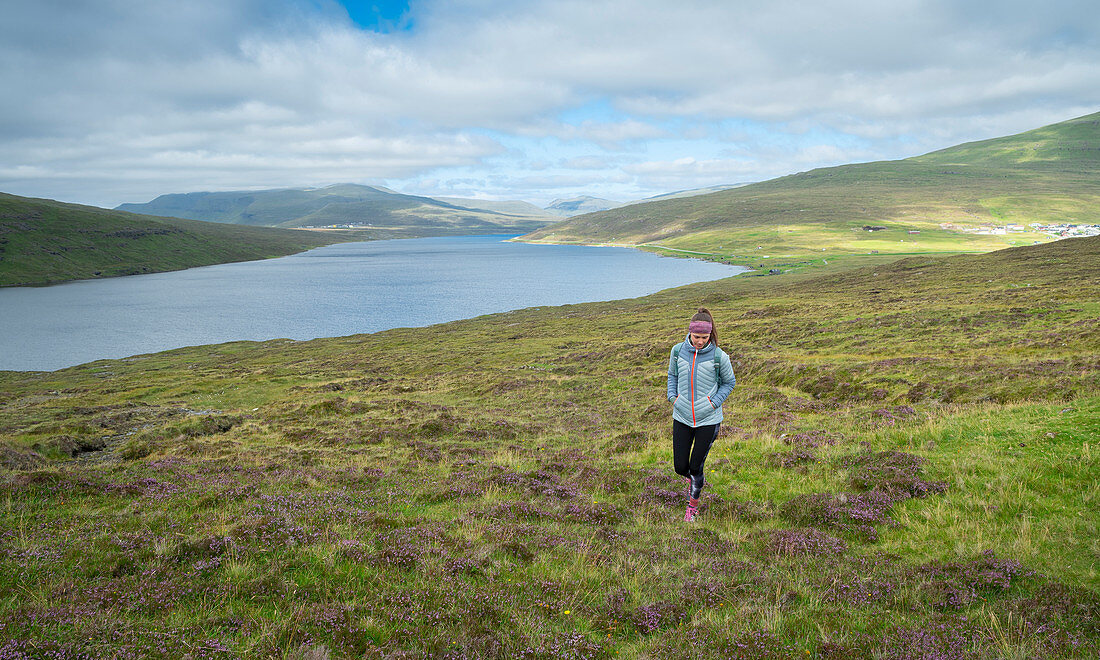 Woman hikes by the Leitisvatn lake near Trælanípa on the island of Vagar, Faroe Islands