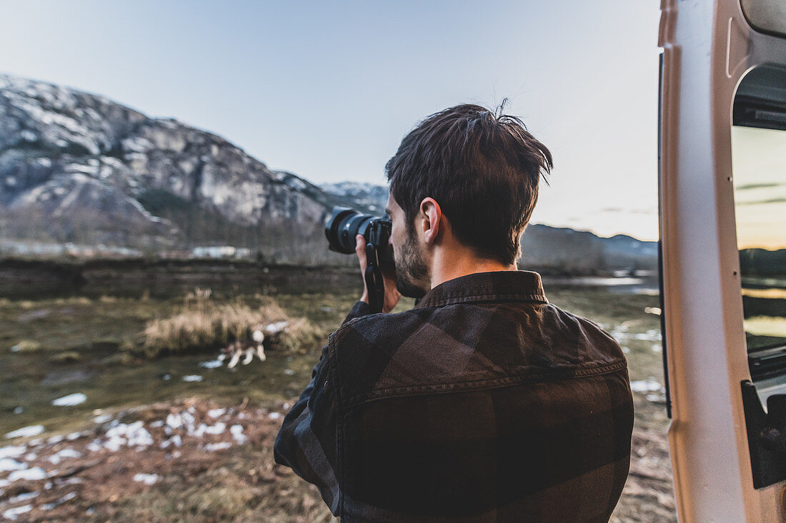 Man standing beside his van taking a picture of a rocky landscape.