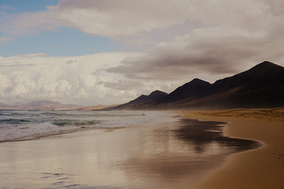 Blick entlang eines Sandstrandes auf Fuerteventura an einem wolkigen Tag.