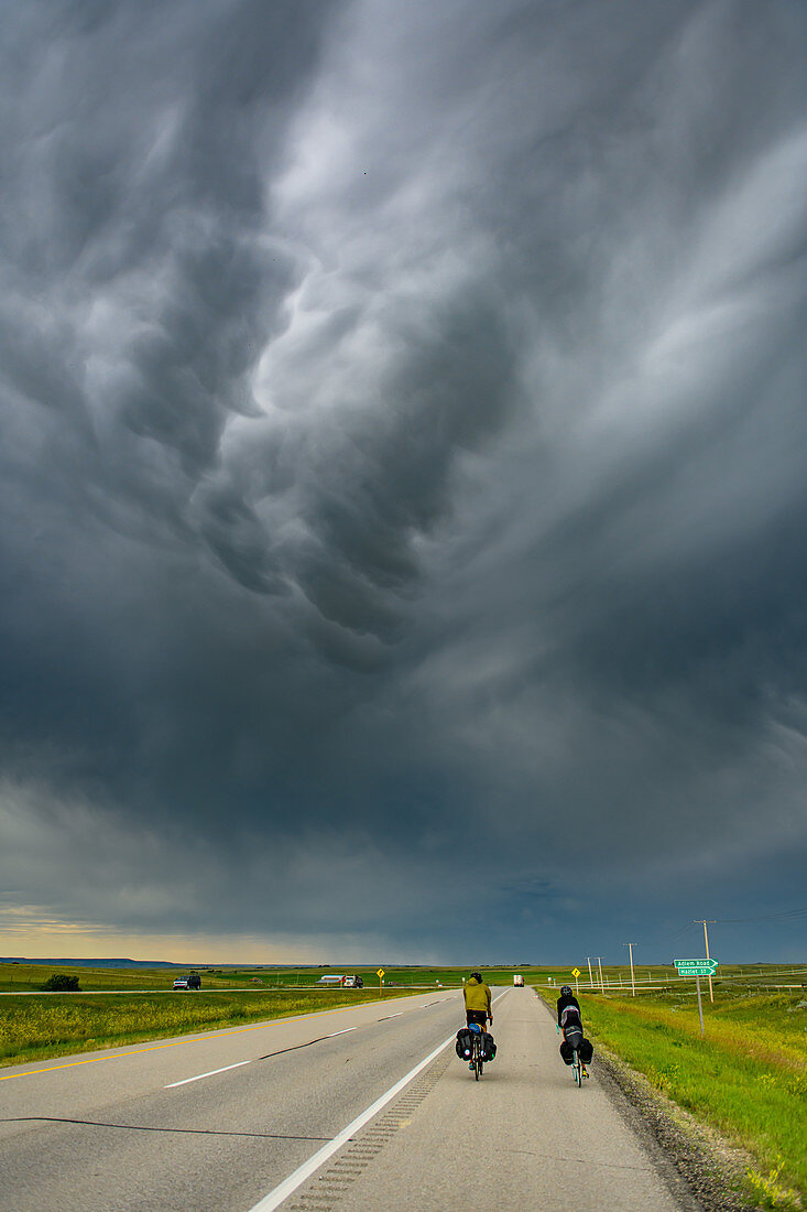 Cyclists on road under a stormy sky, Ontario, Canada