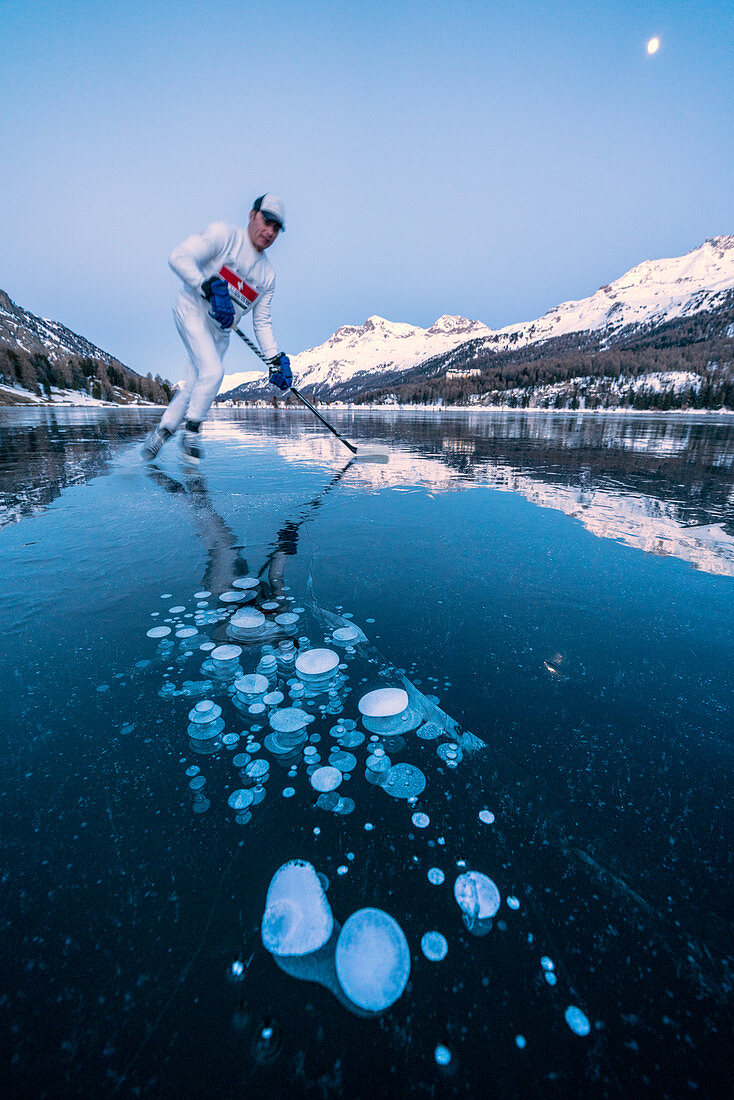 Eishockeyspieler-Mann, der auf See Sils läuft, bedeckt in den Eisblasen in der Abenddämmerung, Engadin, Kanton Graubunden, Schweiz, Europa
