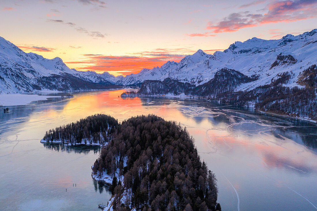 Aerial view of burning sky at sunset on frozen Lake Sils and snow capped mountains, Maloja Pass, Graubunden canton, Swiss Alps, Switzerland, Europe