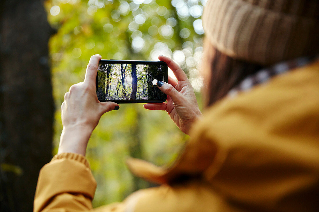 Woman holding up smart phone taking photograph of trees