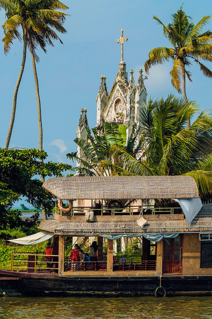 Old church with patinated facade and moored houseboat on a backwaters cruise visitor stop, Alappuzha (Alleppey), Kerala, India, Asia