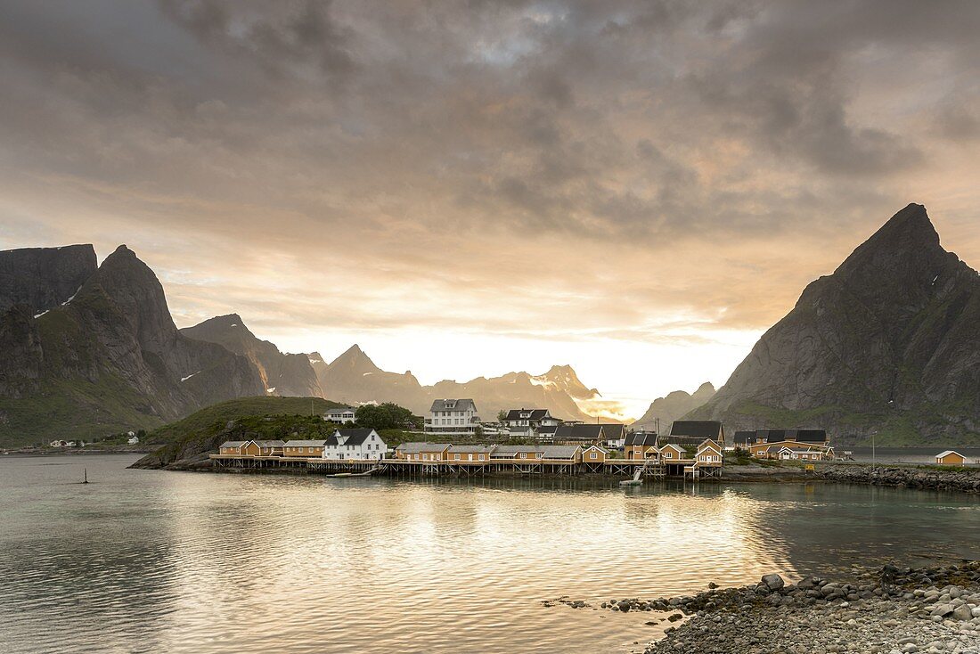 Mitternachtssonne auf den Fischerdorfrahmen durch felsige Gipfel und Meer Sakrisoya, Nordland Grafschaft, Lofoten-Inseln, Nordnorwegen, Europa