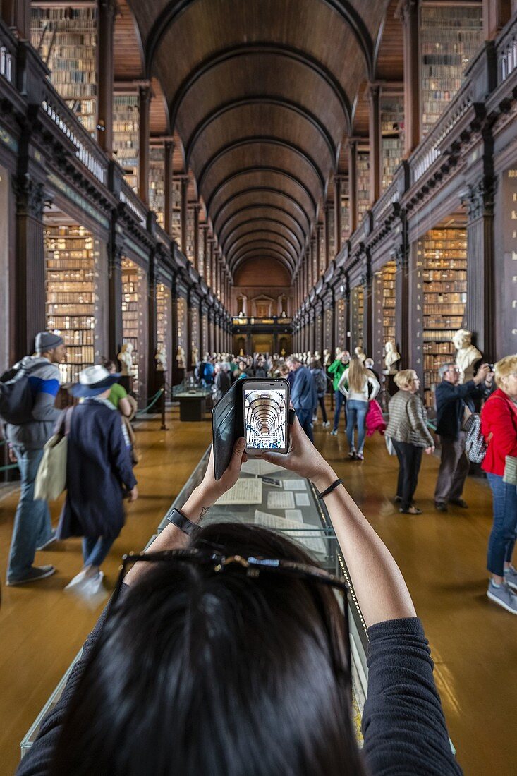 Ansicht eines Touristen, der Bilder mit einem Smartphone des Innenraums der Trinity College-Bibliothek, Dublin, Irland, Europa macht.