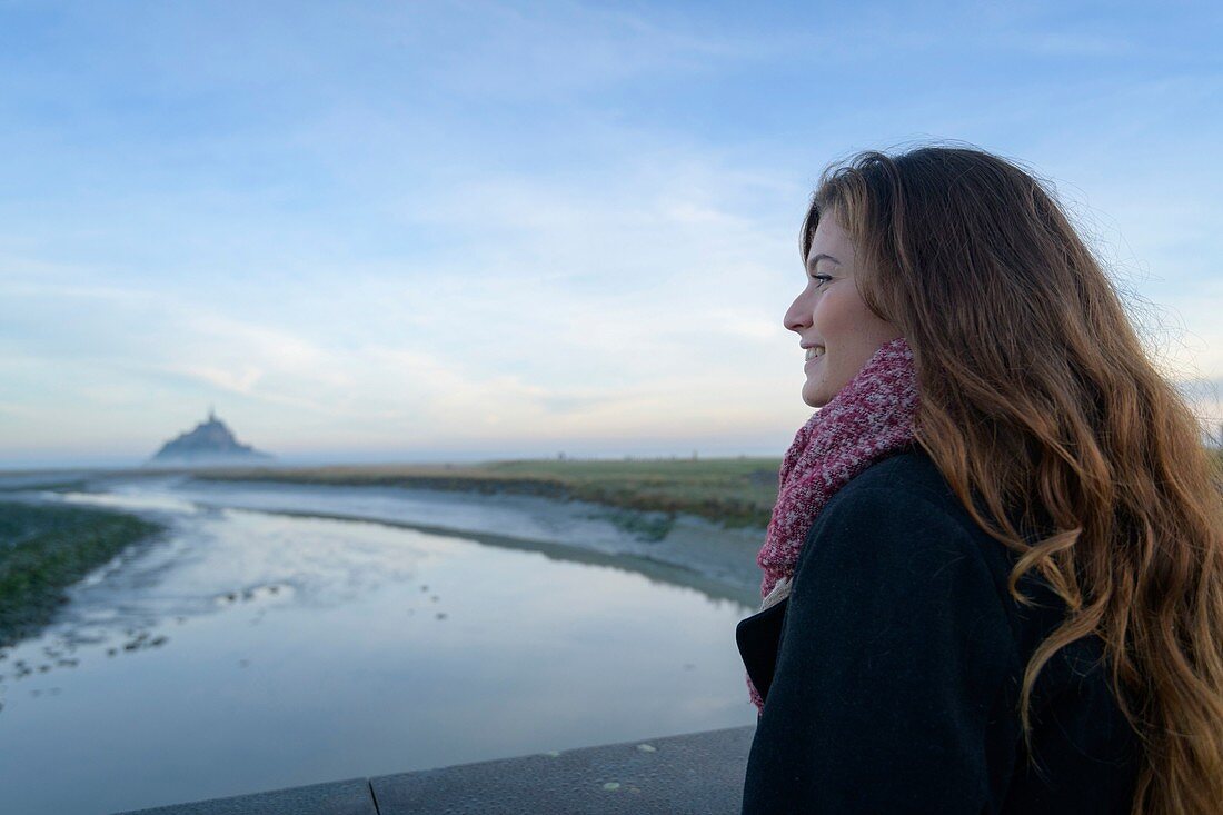 Frankreich, Manche, der Mont-Saint-Michel, junge Frau betrachten die Insel und die Abtei bei Sonnenaufgang von der Mündung des Couesnon