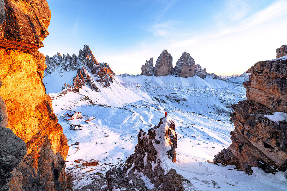 Mann auf Felsen, die den schneebedeckten Monte Paterno und Tre Cime di Lavaredo bei Sonnenuntergang, Sestodolomiten, Südtirol, Italien, Europa bewundern