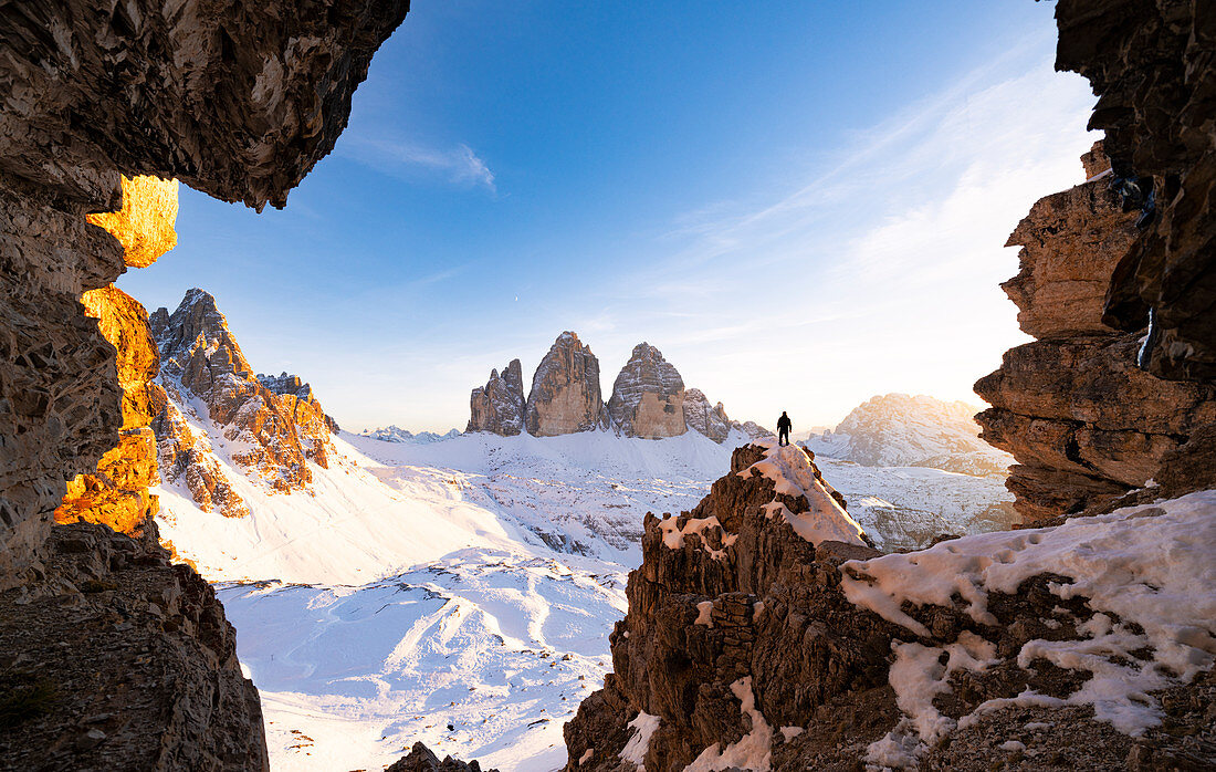 Wanderer auf Felsen, die Tre Cime di Lavaredo und Monte Paterno bewundern, bedeckt mit Schnee bei Sonnenuntergang, Sestodolomiten, Südtirol, Italien, Europa
