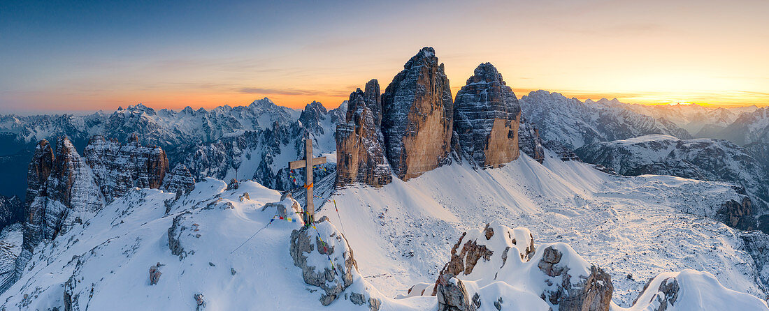 Summit cross on snow capped Monte Paterno with Tre Cime Di Lavaredo in background at sunset, Sesto Dolomites, South Tyrol, Italy, Europe