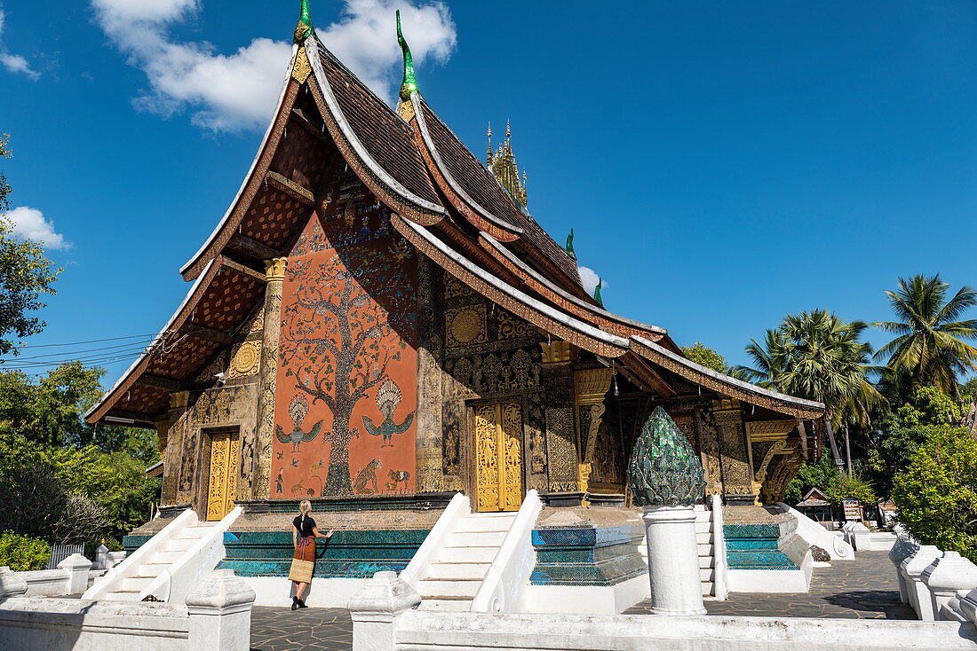 Junge blonde Frau bewundert das Dekor am buddhistischen Tempel Wat Xieng Thong (Tempel der goldenen Stadt), Luang Prabang, Provinz Luang Prabang, Laos, Asien