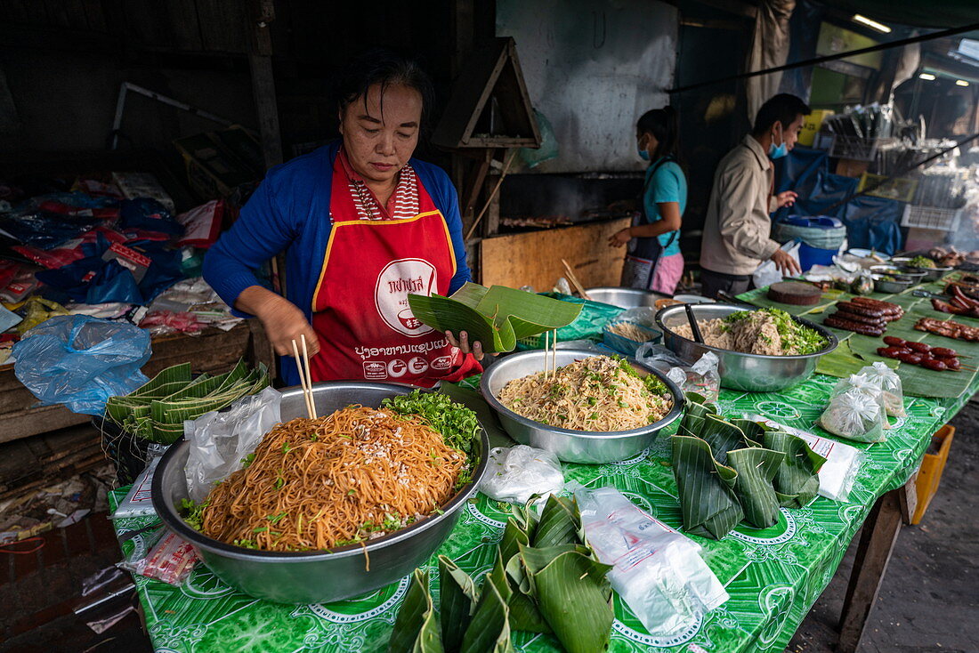 Frau bereitet in Bananenblättern eingewickelte Delikatessen zum Verkauf am Morgenmarkt vor, Luang Prabang, Provinz Luang Prabang, Laos, Asien