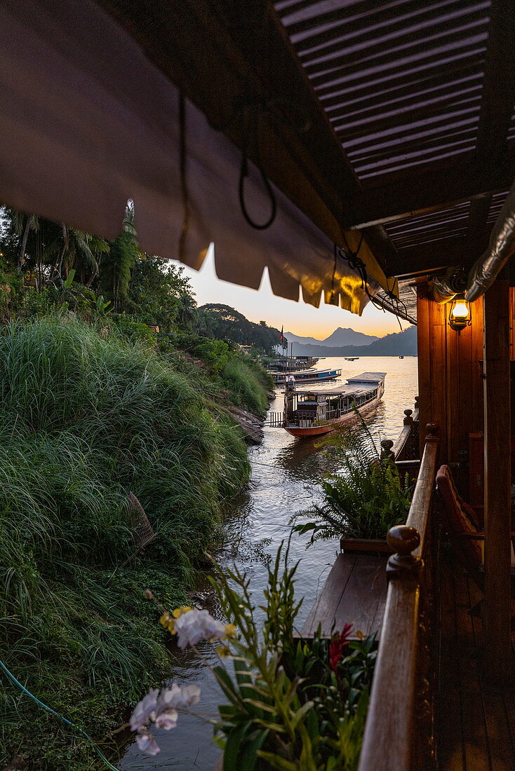 Seite von Flusskreuzfahrtschiff Mekong Sun auf Fluss Mekong und Longtail-Boot in der Abenddämmerung, Luang Prabang, Provinz Luang Prabang, Laos, Asien