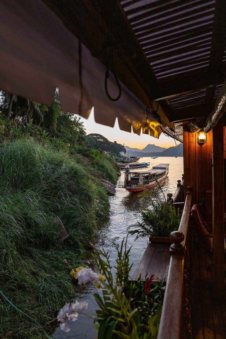 Side of river cruise ship Mekong Sun on river Mekong and longtail boat at dusk, Luang Prabang, Luang Prabang Province, Laos, Asia