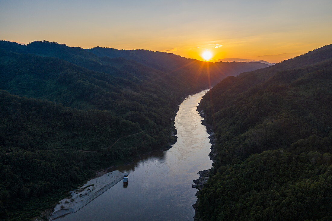 Luftaufnahme von Flusskreuzfahrtschiff Mekong Sun am sandigen Ufer des Mekong mit Bergen bei Sonnenuntergang, Ban Hoy Palam, Bezirk Pak Tha, Provinz Bokeo, Laos, Asien