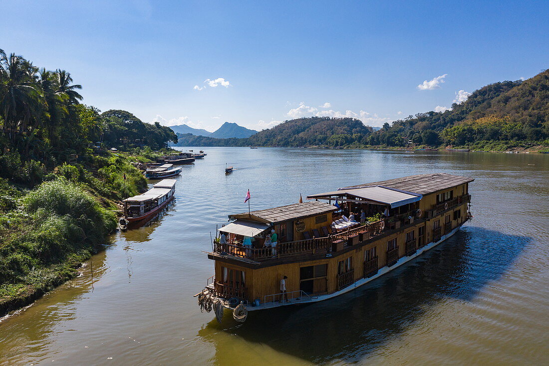Luftaufnahme von Flusskreuzfahrtschiff Mekong Sun und lokaler Ausflugsboote am Ufer vom Fluss Mekong, Luang Prabang, Provinz Luang Prabang, Laos, Asien