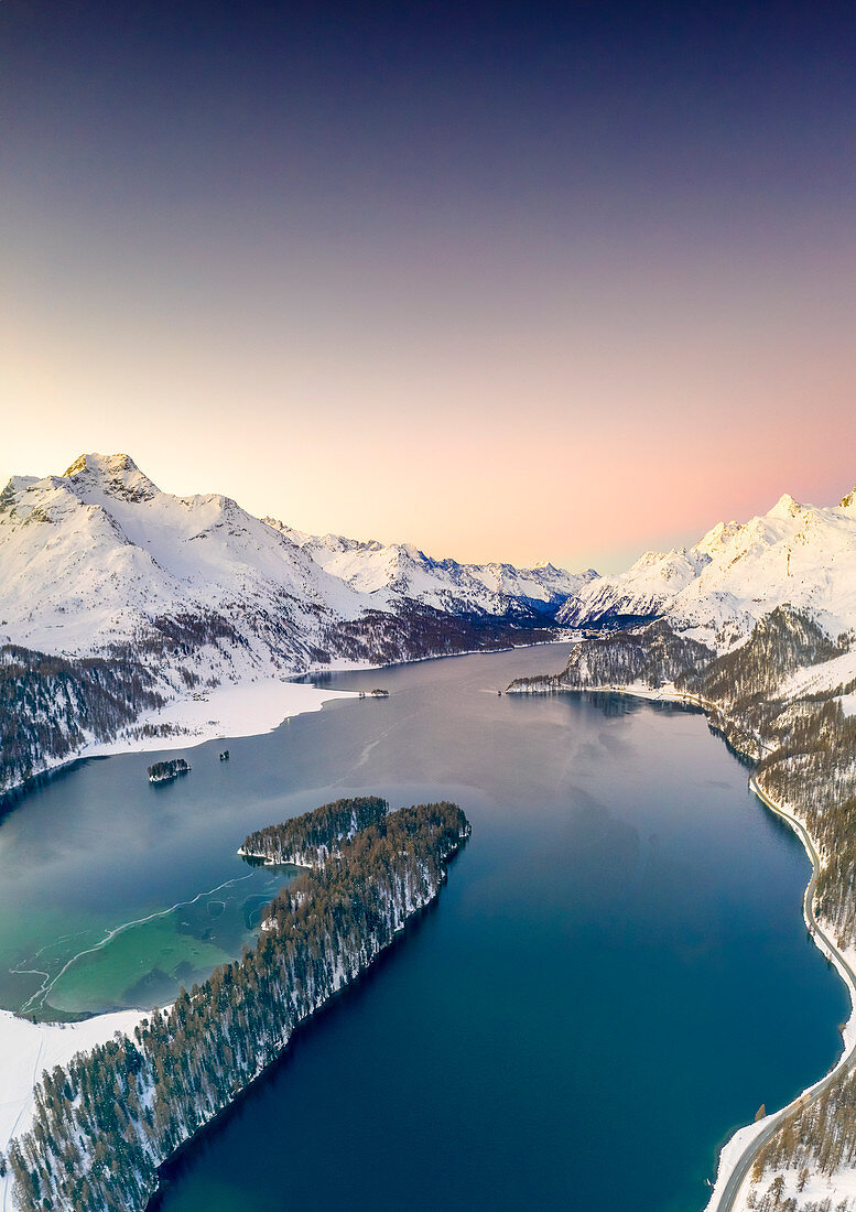 Luftaufnahme durch Drohne des schneebedeckten Piz Da La Margna und des Sils-Sees bei Sonnenaufgang, Engadin, Kanton Graubunden, Schweiz, Europa