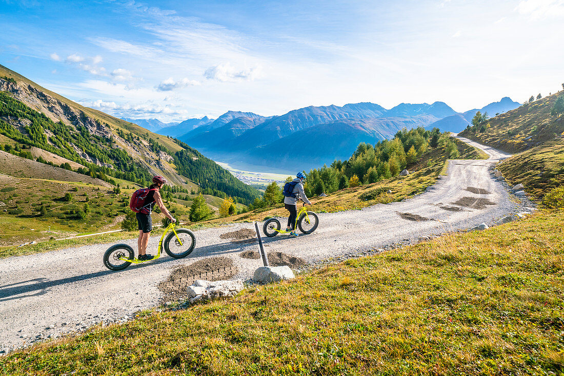Two people having fun riding the Trottinett scooters downhill from Marguns top station to Celerina, Engadine, canton of Graubunden, Switzerland, Europe