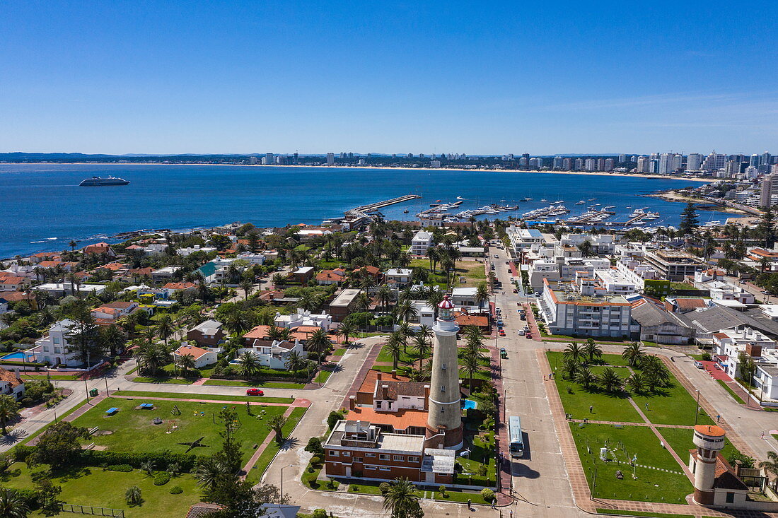 Luftaufnahme von Leuchtturm Faro de Punta del Este mit Stadt und Expeditions Kreuzfahrtschiff World Explorer (nicko cruises) in der Ferne, Punta del Este, Maldonado Department, Uruguay, Südamerika