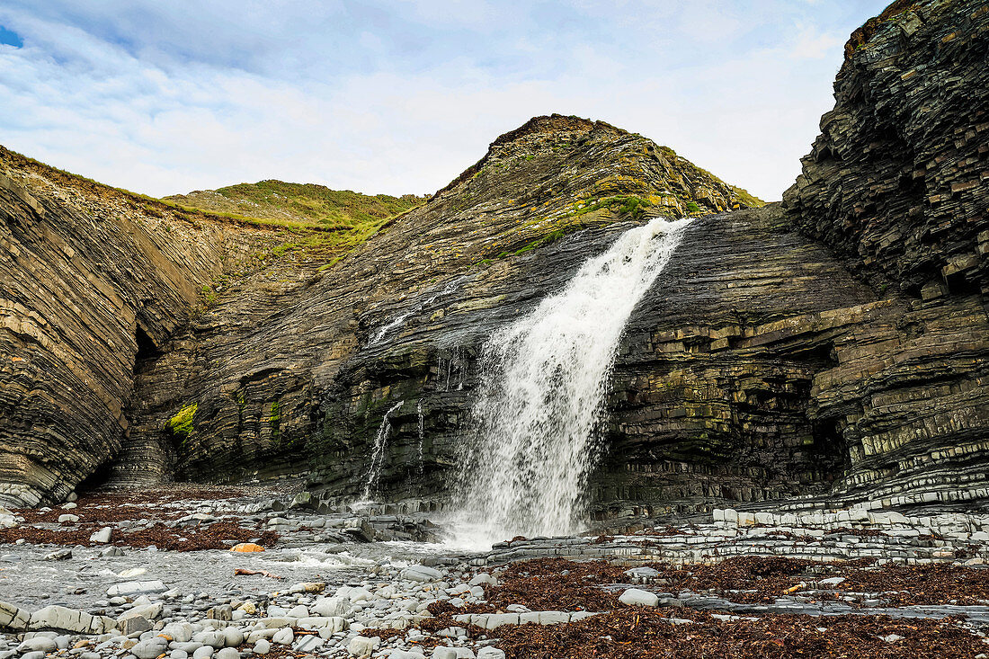 Ungewöhnlicher Strandwasserfall, wo der Afon Drywi über silurische Körner in Little Quay Bay, New Quay, Ceredigion, Wales, Vereinigtes Königreich, Europa stürzt