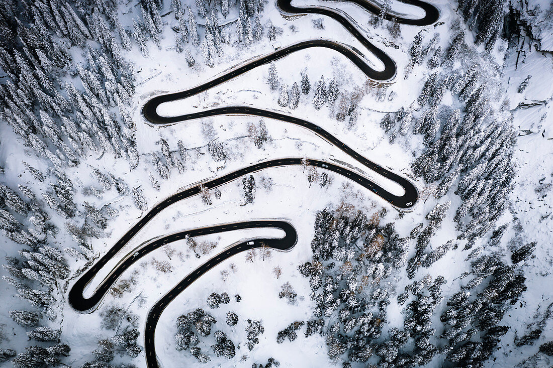 Aerial view of cars on narrow bends of mountain road crossing the snowy forest, Switzerland, Europe