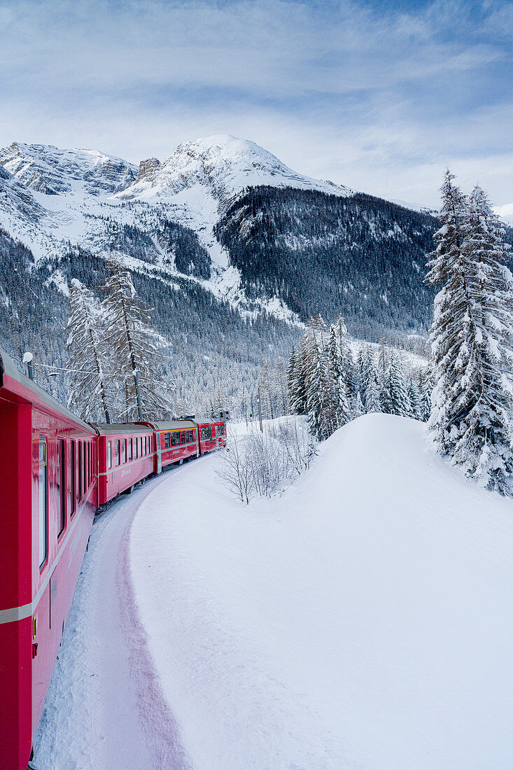 Roter Bernina Expresszug, der die verschneite Landschaft im Winter, Preda Bergun, Albula-Tal, Kanton Graubunden, Schweiz, Europa kreuzt