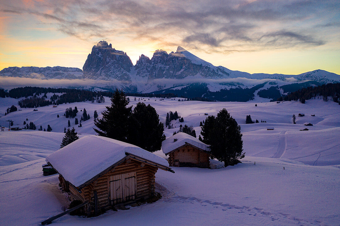 Wood cabins covered with snow with Sassopiatto and Sassolungo in background at dawn, Seiser Alm, Dolomites, South Tyrol, Italy, Europe