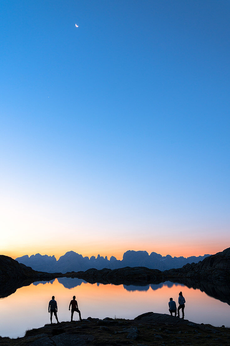 Wanderer, die die Dolomiten der Brenta-Gruppe bewundern, spiegeln sich im Lago Nero di Cornisello im Morgengrauen, Trento, Trentino-Südtirol, Italien, Europa