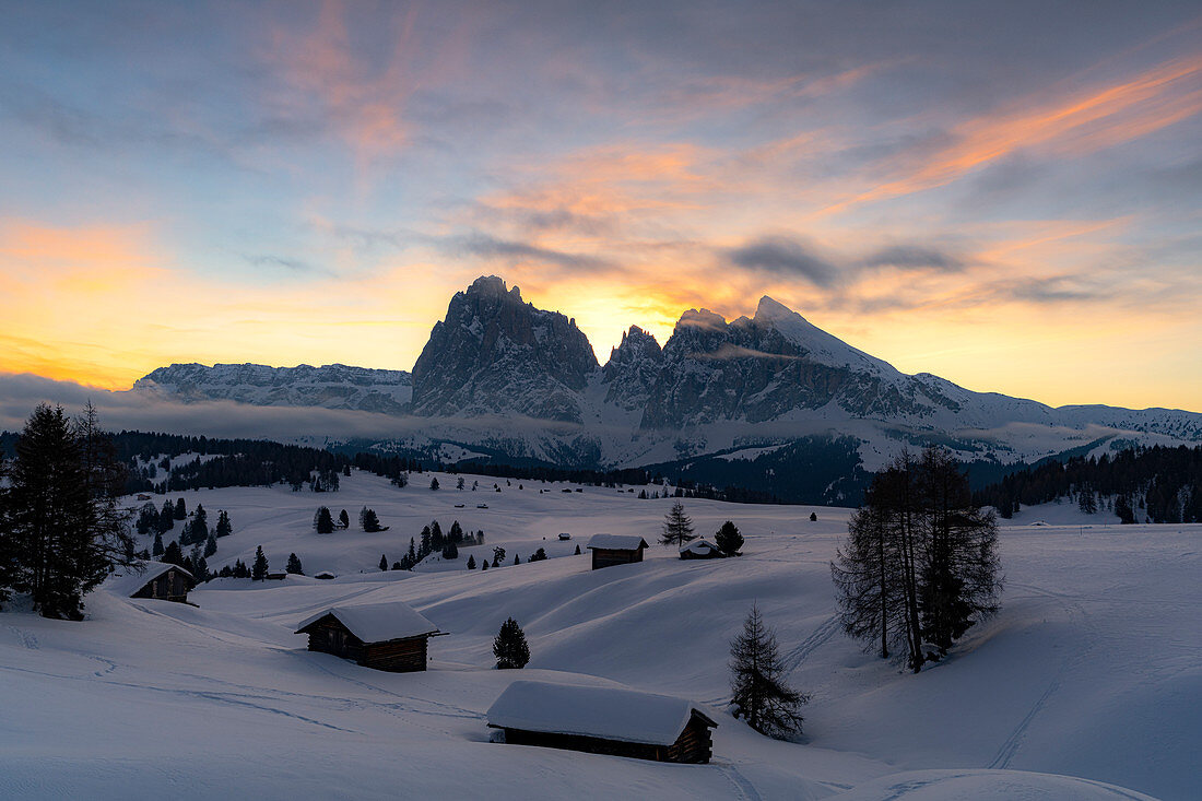 Berghütten bedeckt mit Schnee mit Sassopiatto und Sassolungo im Hintergrund im Morgengrauen, Seiser Alm, Dolomiten, Südtirol, Italien, Europa
