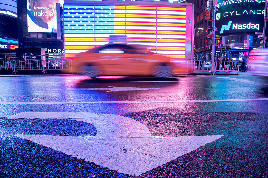 Taxi blurring by an illuminated flag of the United States of America at Times Square, New York City, United States of America, North America