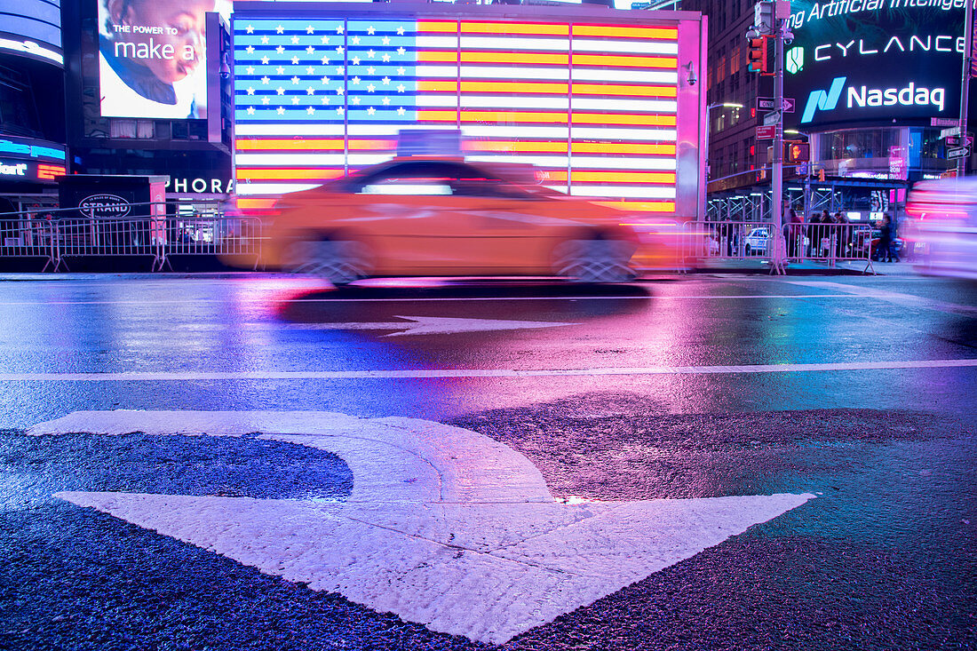 Taxi, das durch eine beleuchtete Flagge der Vereinigten Staaten von Amerika am Times Square, New York City, Vereinigte Staaten von Amerika, Nordamerika verwischt