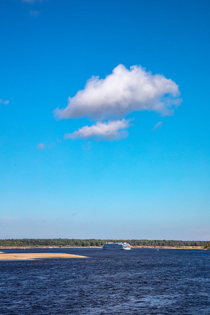 Weiße Wolke im blauen Himmel mit Flusskreuzfahrtschiff auf Fluss Wolga in der Ferne, nahe Nischni Nowgorod, Bezirk Nischni Nowgorod, Russland, Europa